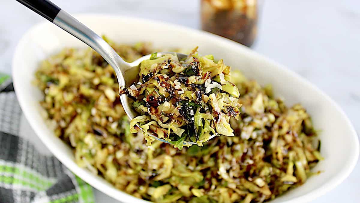 Shredded Brussels Sprouts held up in spoon over white bowl