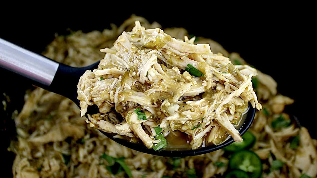 Slow Cooker Salsa Verde Chicken in black serving spoon held up over slow cooker