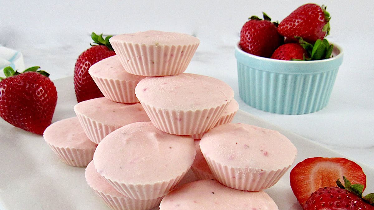 Strawberry Cheesecake Fat Bombs stacked with strawberries in background