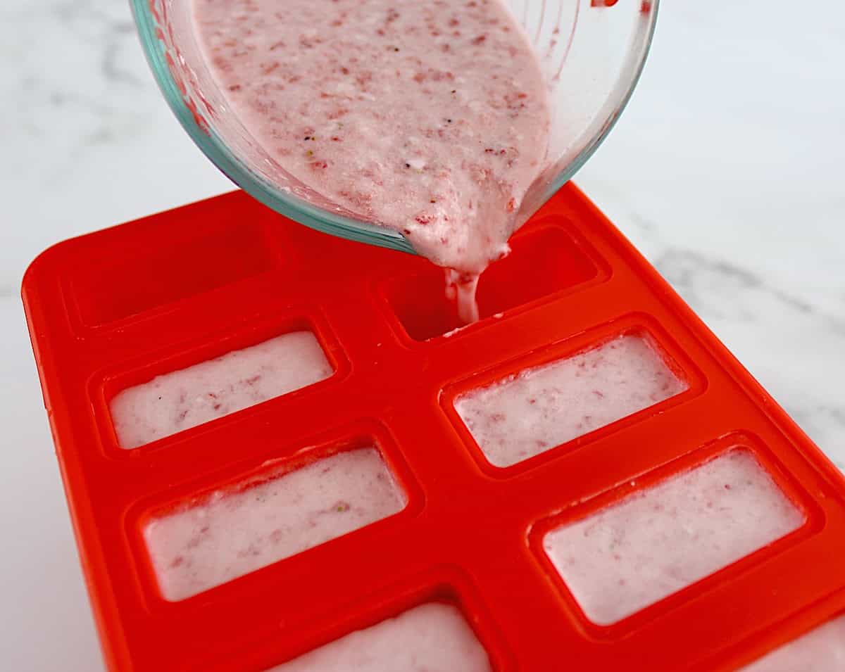 Strawberry Coconut Cream Popsicles mixture being poured into red popsicle mold