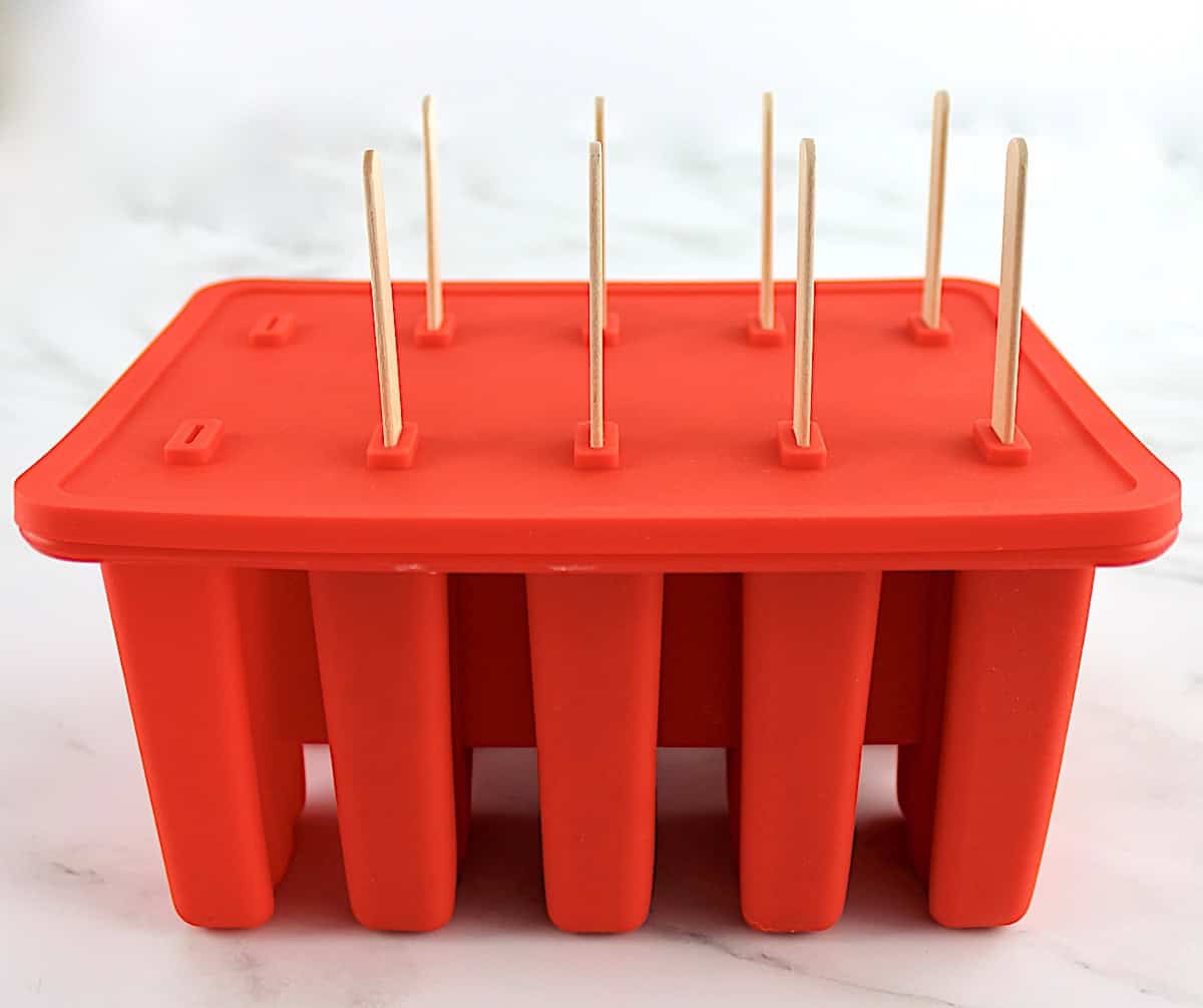 Strawberry Coconut Cream Popsicles in red molds with cover and 8 popsicle sticks