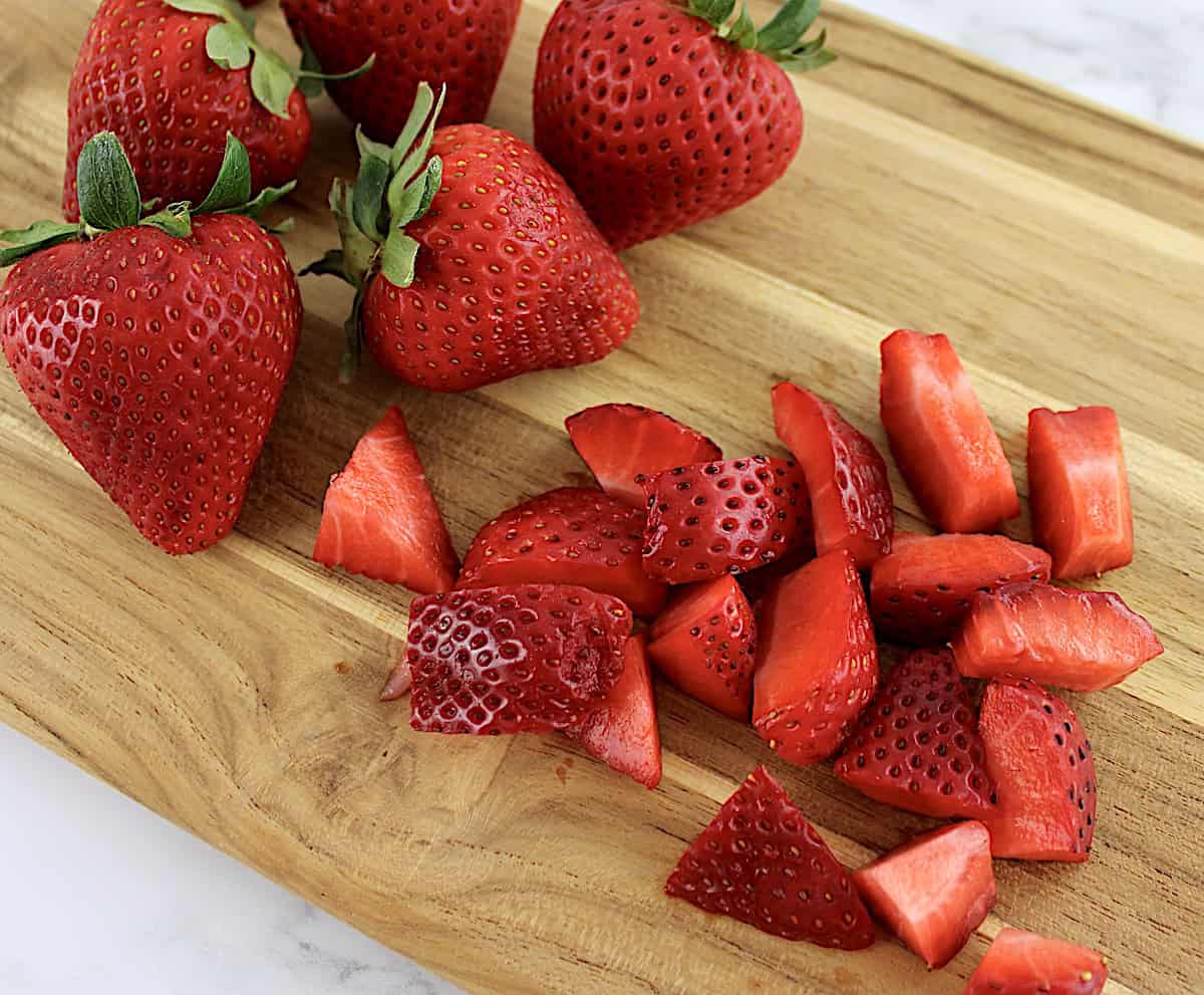 chopped strawberries on cutting board with whole strawberries in back