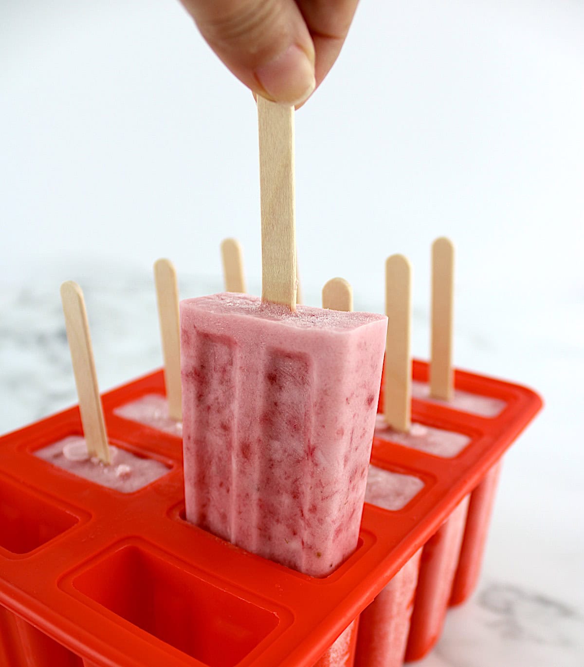 8 Strawberry Coconut Cream Popsicles in red popsicle mold with front popsicle being pulled up