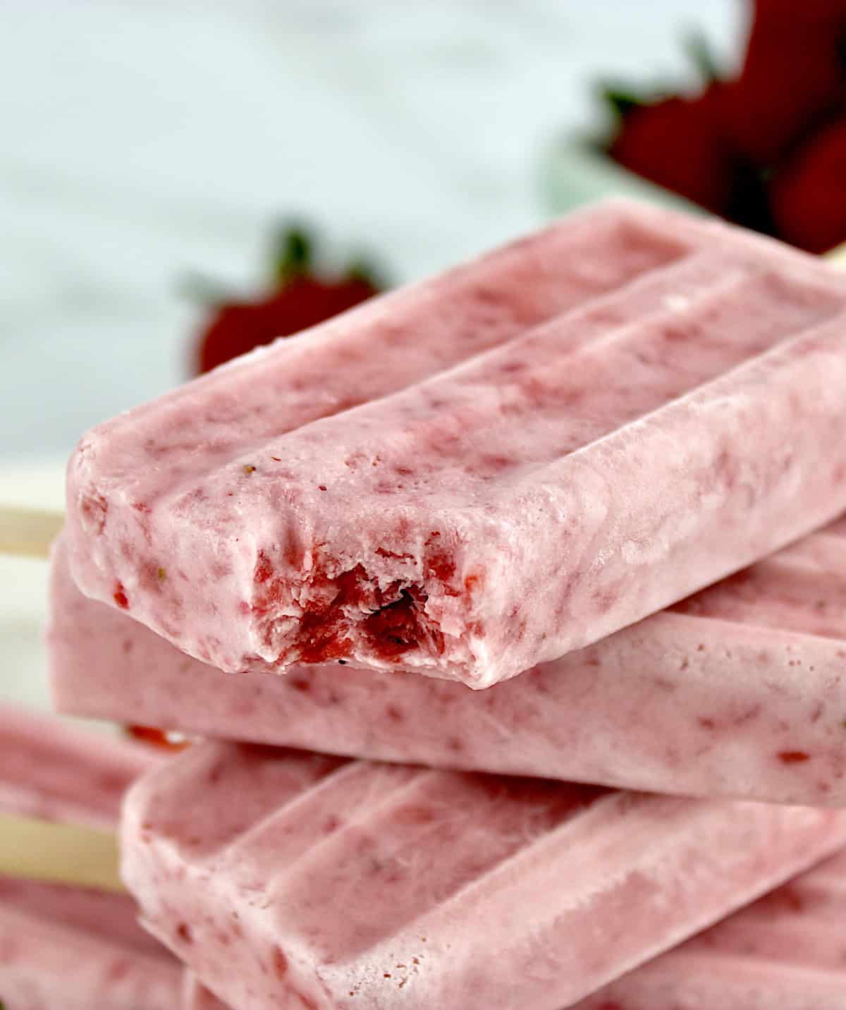 closeup of Strawberry Coconut Cream Popsicles stacked up with bite taken out of top popsicle