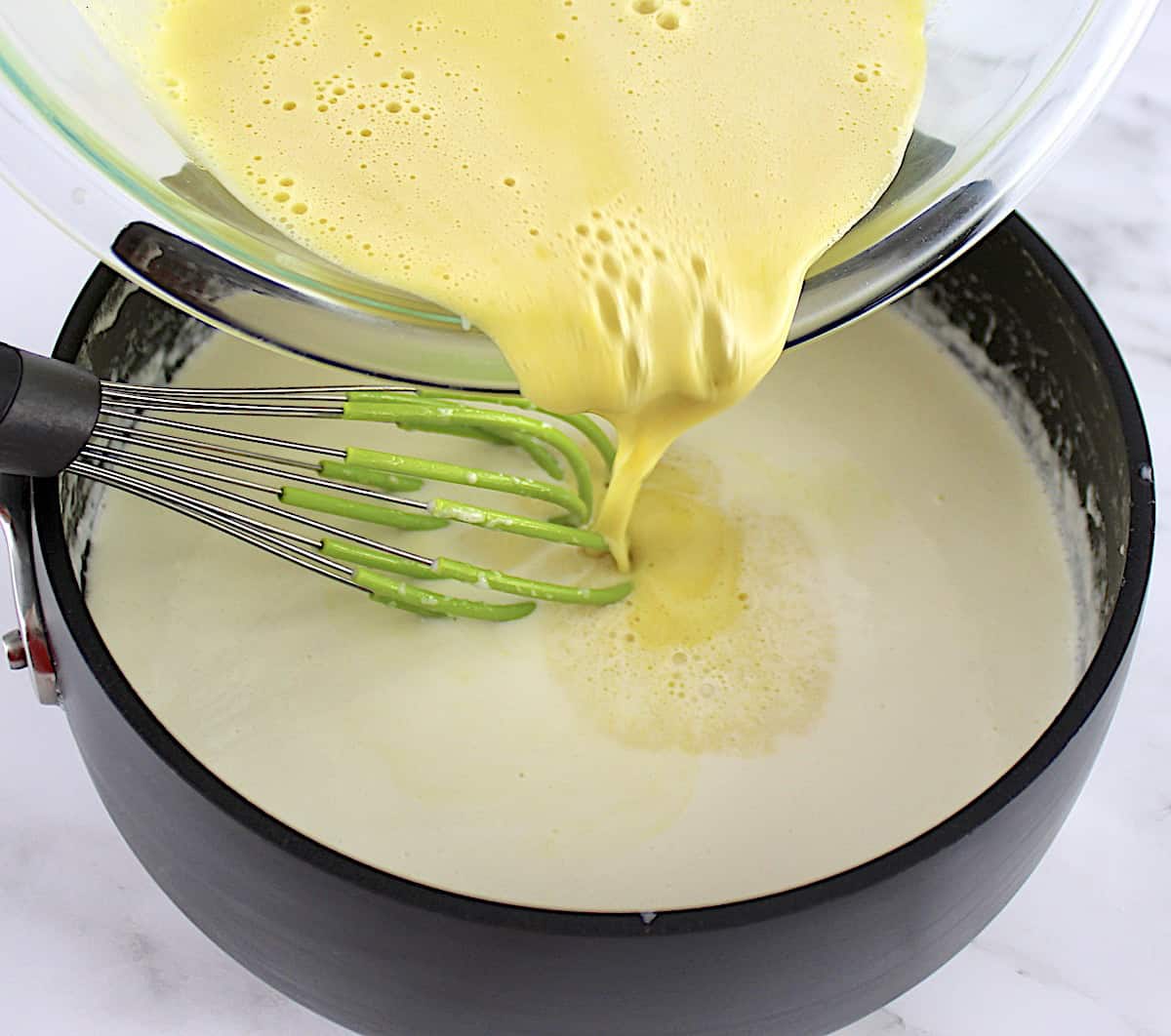 egg yolk and sweetener being poured and whisked into cream in saucepan