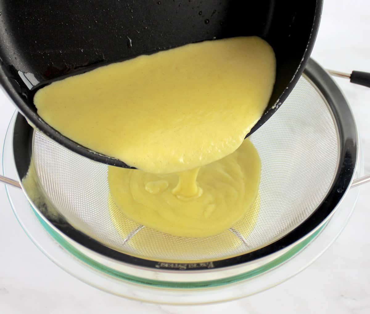 Sugar Free Keto Custard being poured from saucepan through fine mesh sieve