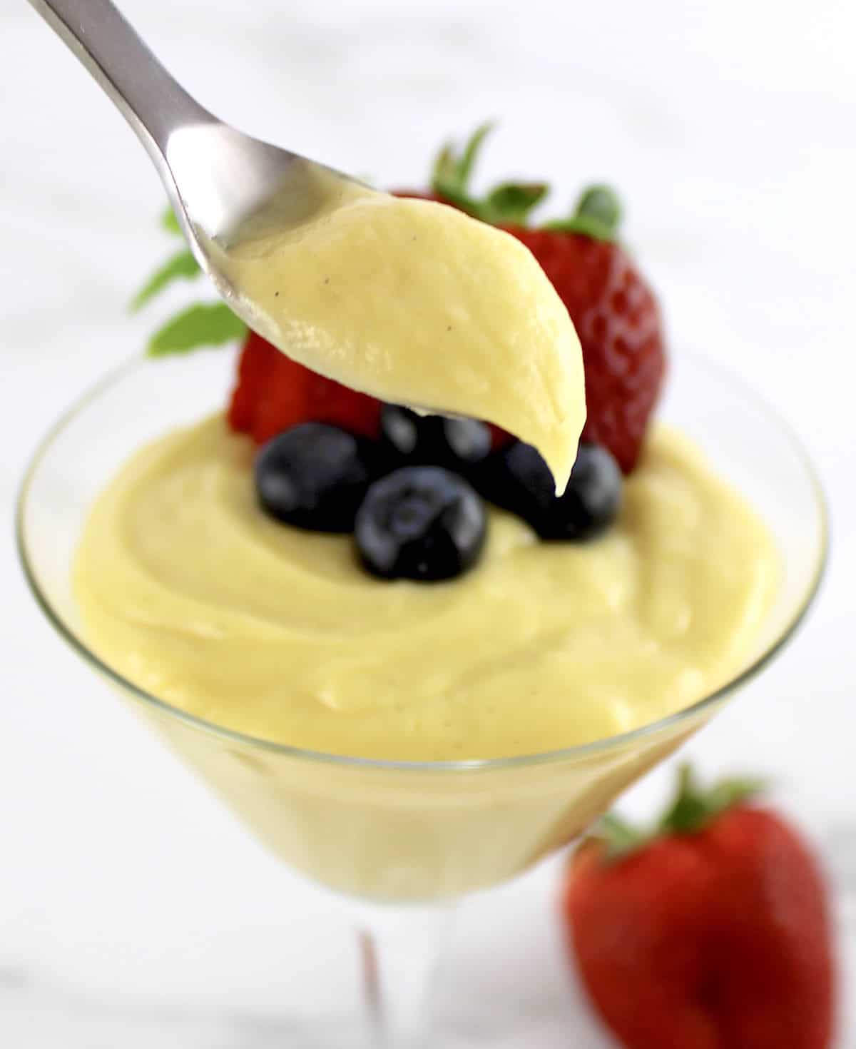 Sugar Free Keto Custard dripping off spoon with custard and berries in glass behind