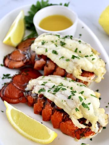 2 Air Fryer Lobster Tails on white oval plate with melted butter and lemon wedges