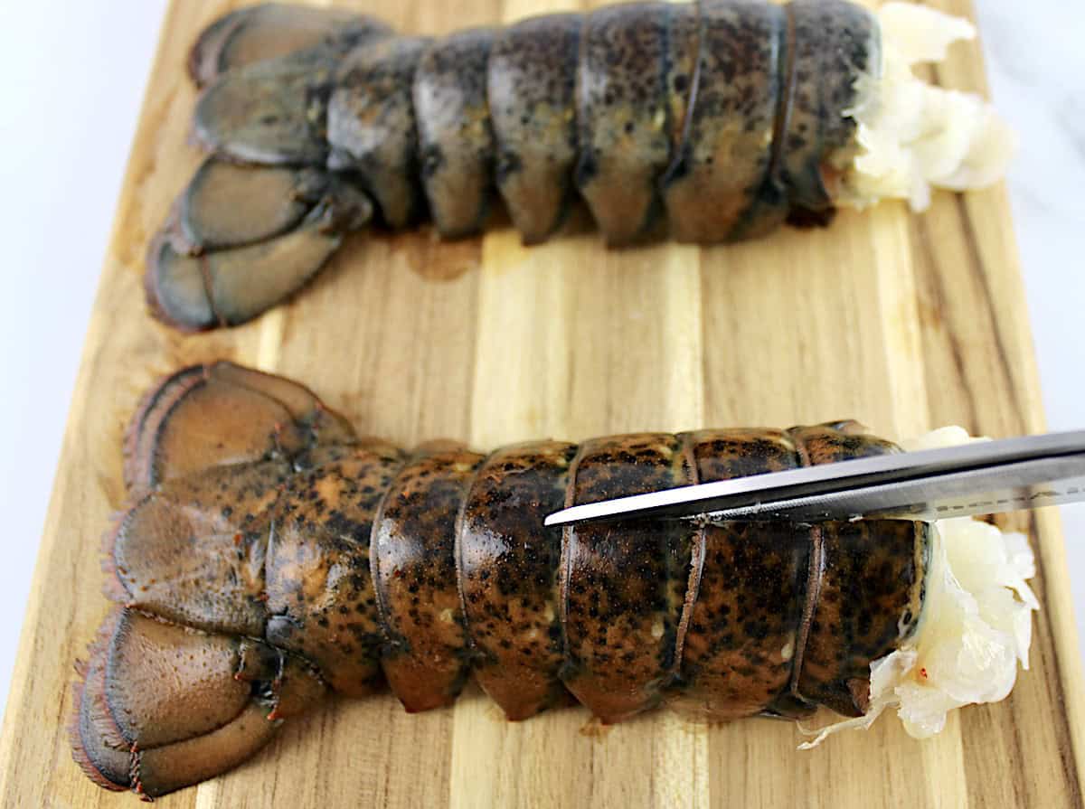 lobster tail on cutting board being cut open with scissors