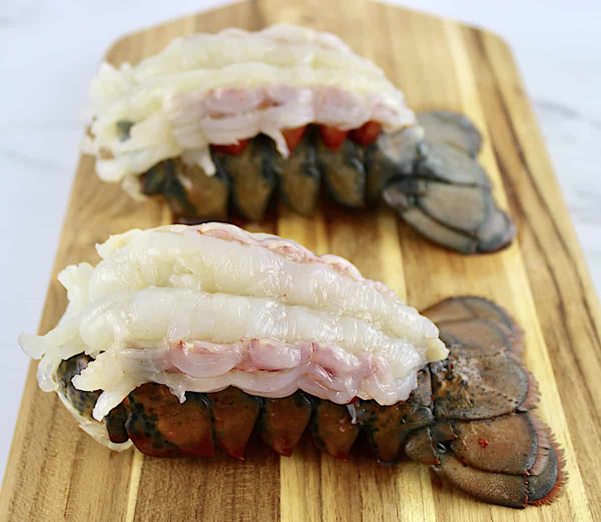 2 raw lobster tails on cutting board with the meat sitting on top