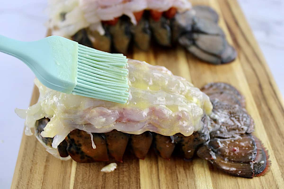 melted butter being brushed over raw lobster tails