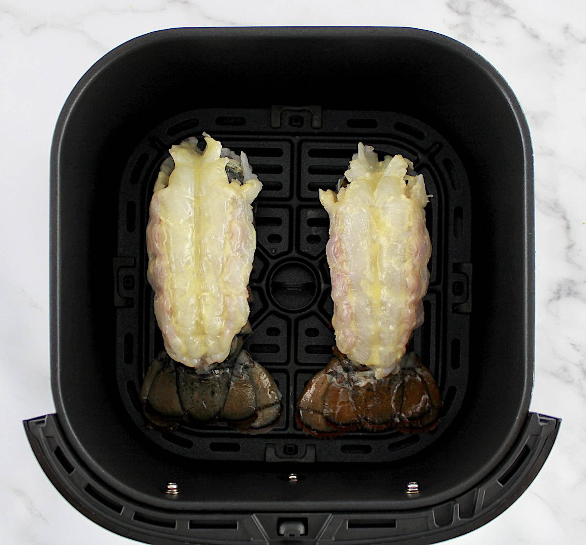 2 raw lobster tails in air fryer with butter brushed on top