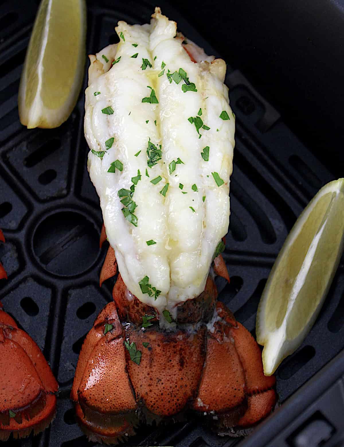 Air Fryer Lobster Tail in air fryer basket with parsley on top and lemon wedges on the side