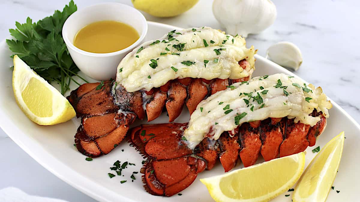 2 Air Fryer Lobster Tails on white plate with lemon wedges and melted butter on side