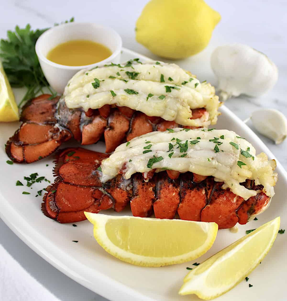 2 Air Fryer Lobster Tails on white plate with lemon wedges and melted butter on side