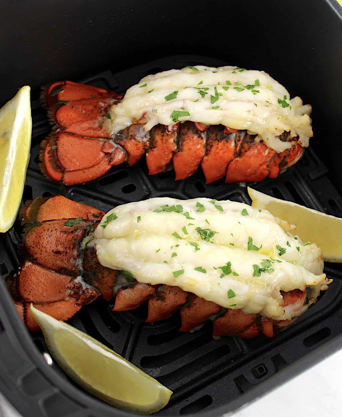 2 Air Fryer Lobster Tails in air fryer basket with lemon wedges