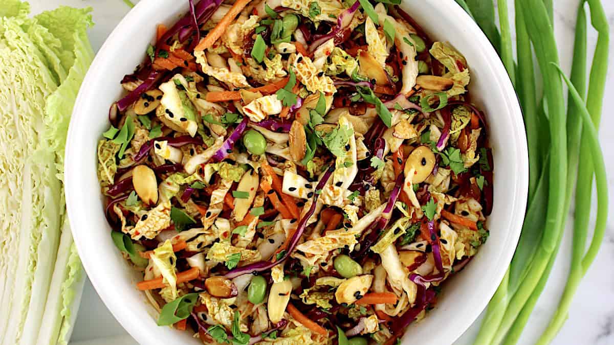 overhead view of Asian Cabbage Slaw in white bowl with scallions on side