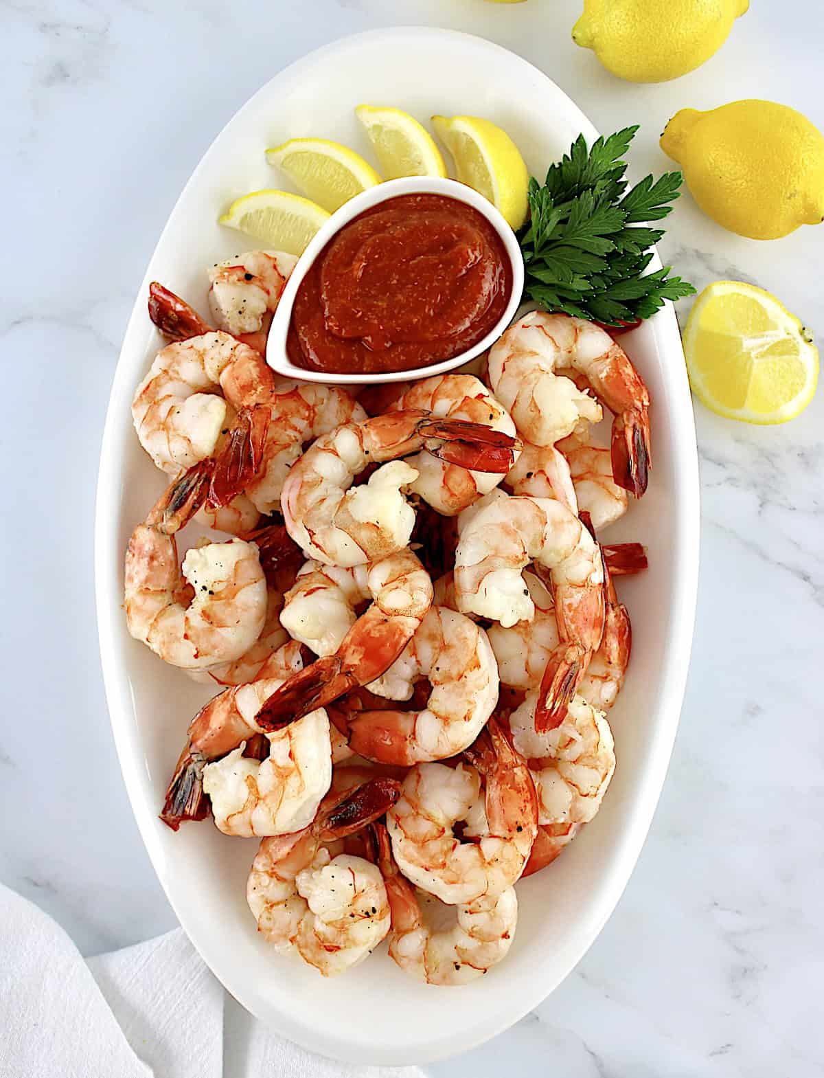 overhead view of Shrimp Cocktail in white oval platter with cocktail sauce and lemon wedges