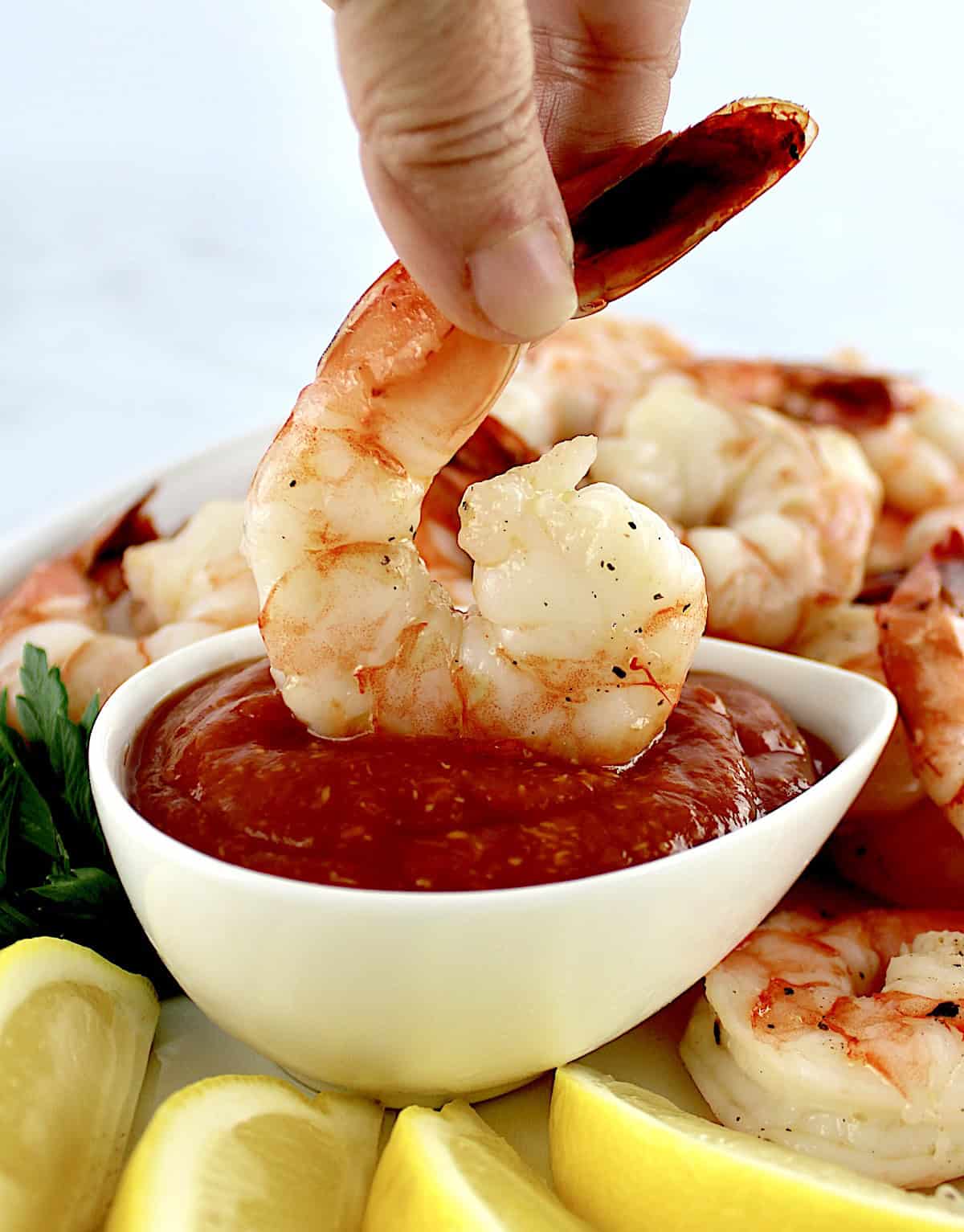 shrimp being dipped in cocktail sauce in white bowl