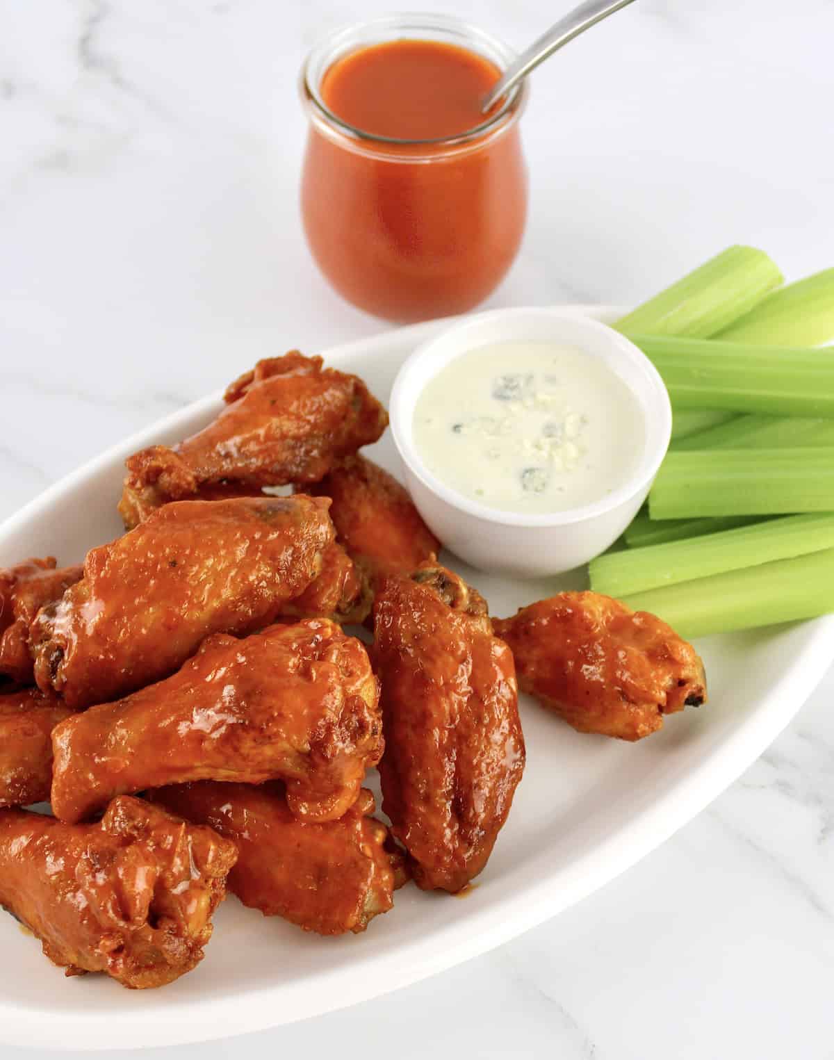 Crispy Air Fryer Buffalo Wings on white plate with bowl of blue cheese dressing and celery sticks
