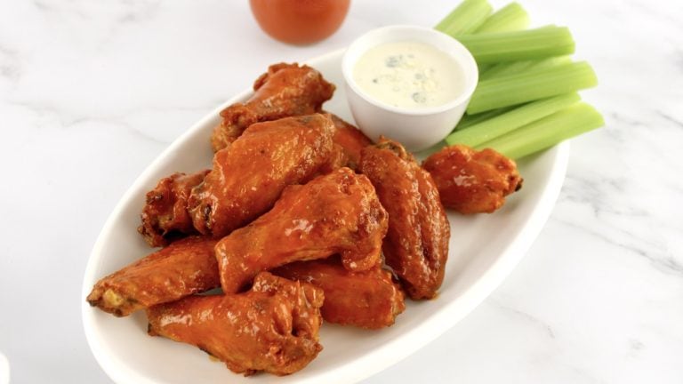 Crispy Air Fryer Buffalo Wings on white plate with bowl of blue cheese dressing and celery sticks