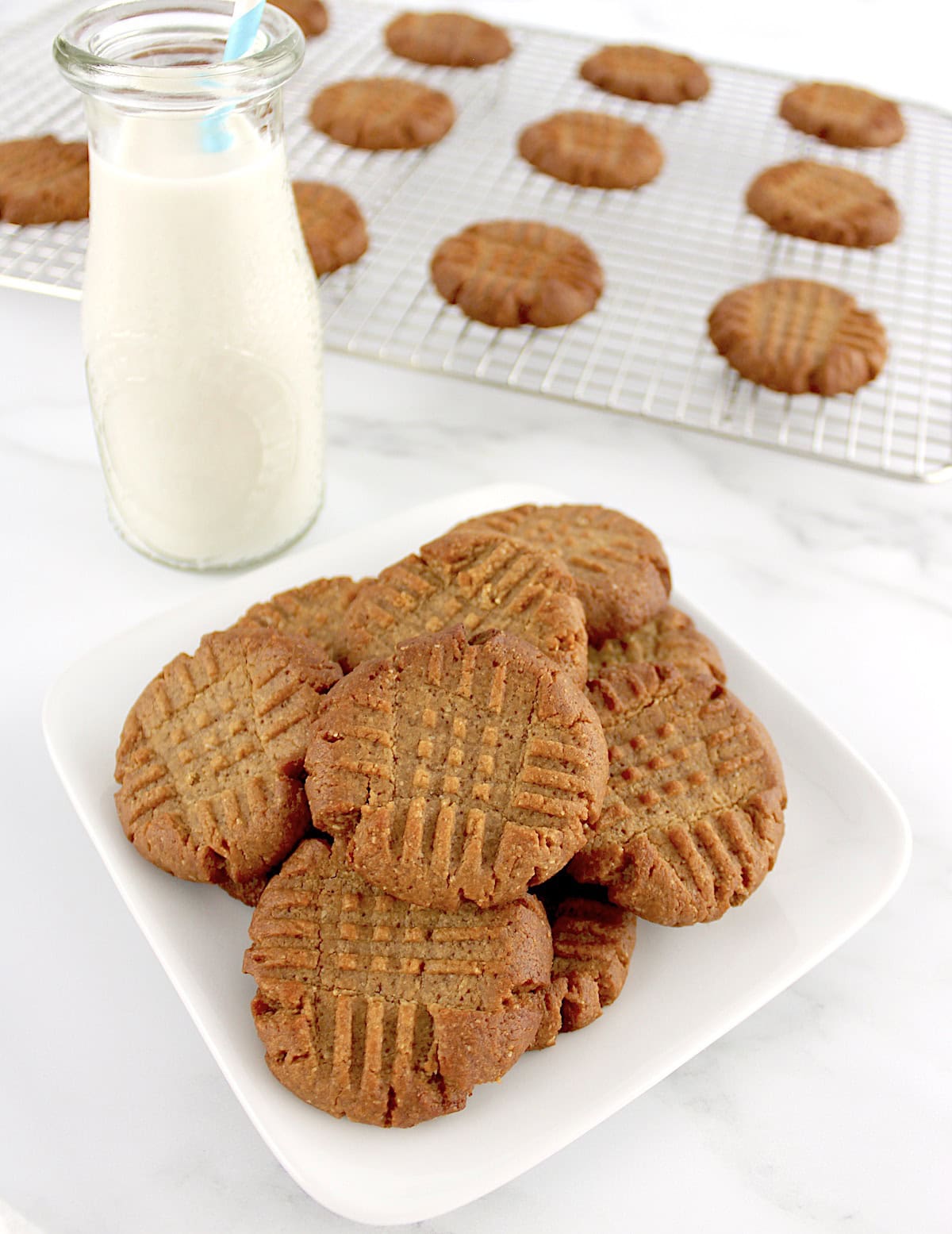 overhead view of Easy Peanut Butter Cookies on white plate with cookies on rack and milk bottle in back