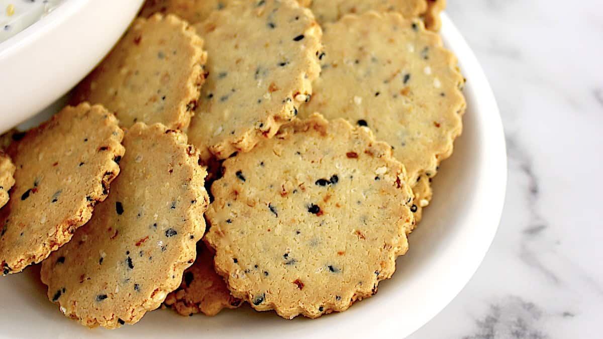 Everything Bagel Crackers on white plate with partial view of dip in white bowl