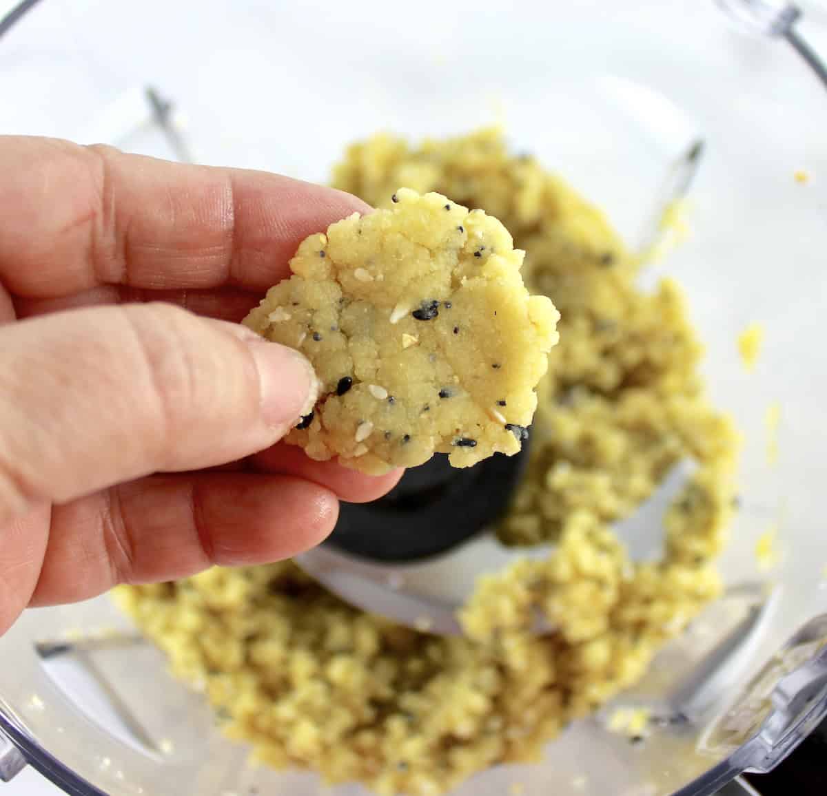 Everything Bagel Crackers dough in food processor bowl with some being pinched in hand