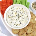 Everything Bagel Dip in white bowl with crackers, celery sticks and carrot chips on white oval platter