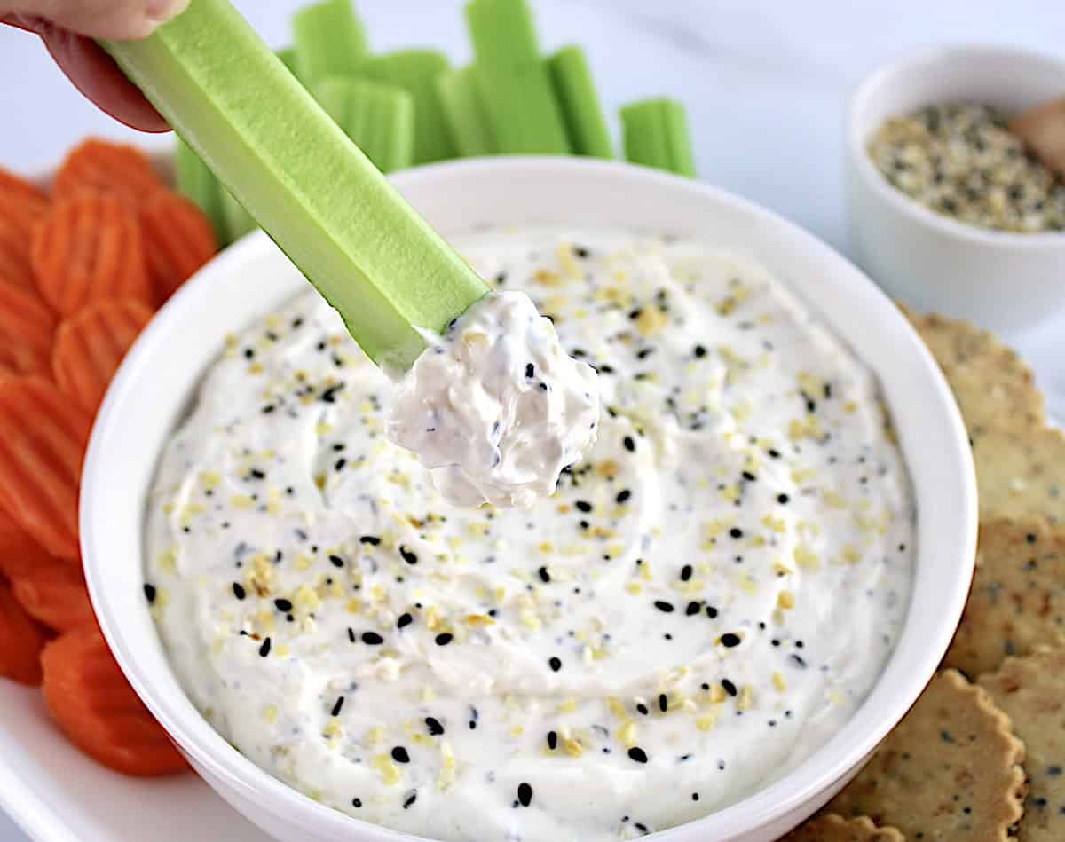 Everything Bagel Dip in white bowl with celery stick dipping into it