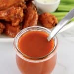 Homemade Buffalo Wing Sauce in open glass jar with wings in background