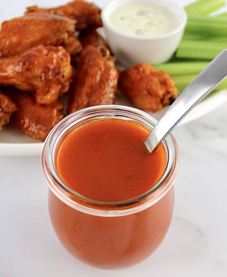 Homemade Buffalo Wing Sauce in open glass jar with wings in background