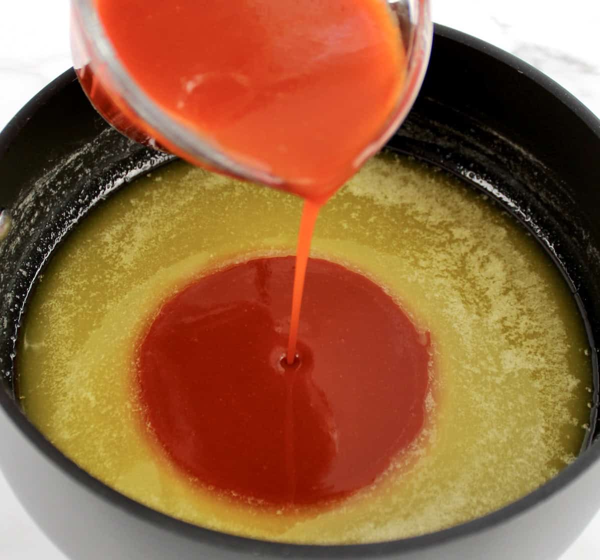 hot sauce being poured into saucepan with melted butter