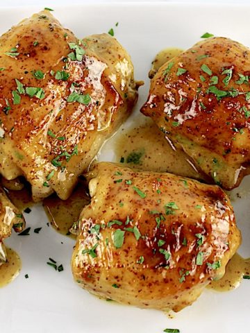 overhead view of Honey Mustard Baked Chicken Thighs on white plate with sauce and chopped parsley on top