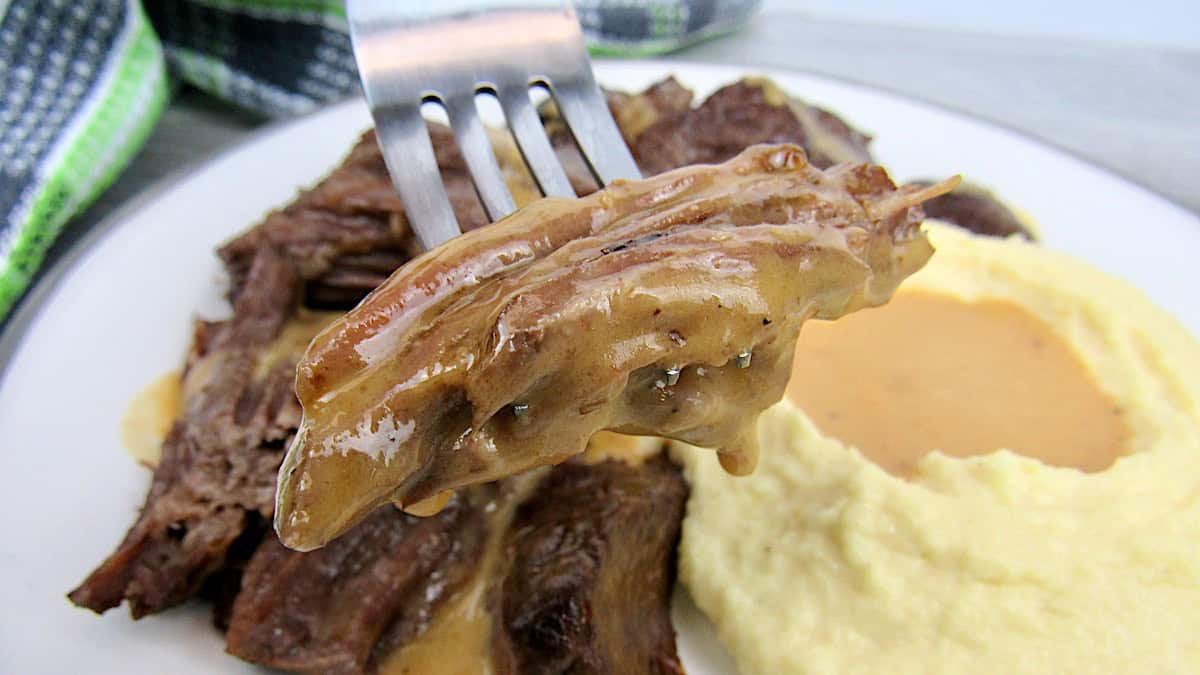 Instant Pot Roast piece on end of fork dripping gravy with mashed cauliflower in back