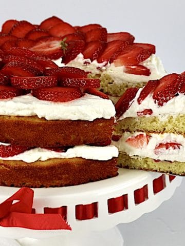 Keto Strawberry Shortcake on white cake stand with slice being removed using silver cake server