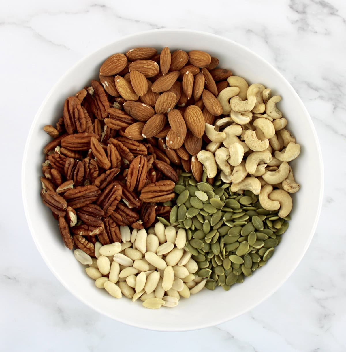 raw peanuts, pecans, pumpkin seeds, cashews and almonds in white bowl in sections