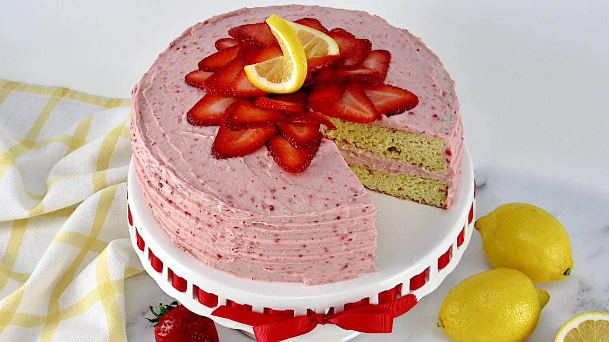 strawberry cake on cake stand with strawberries on top with slice missing