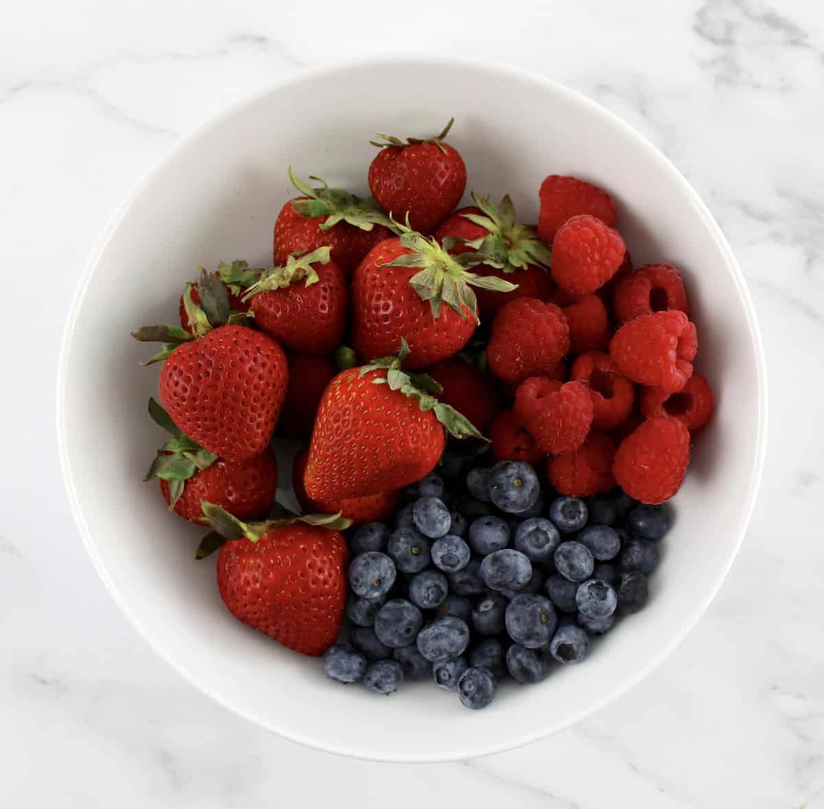 strawberries, raspberries and blueberries in white bowl