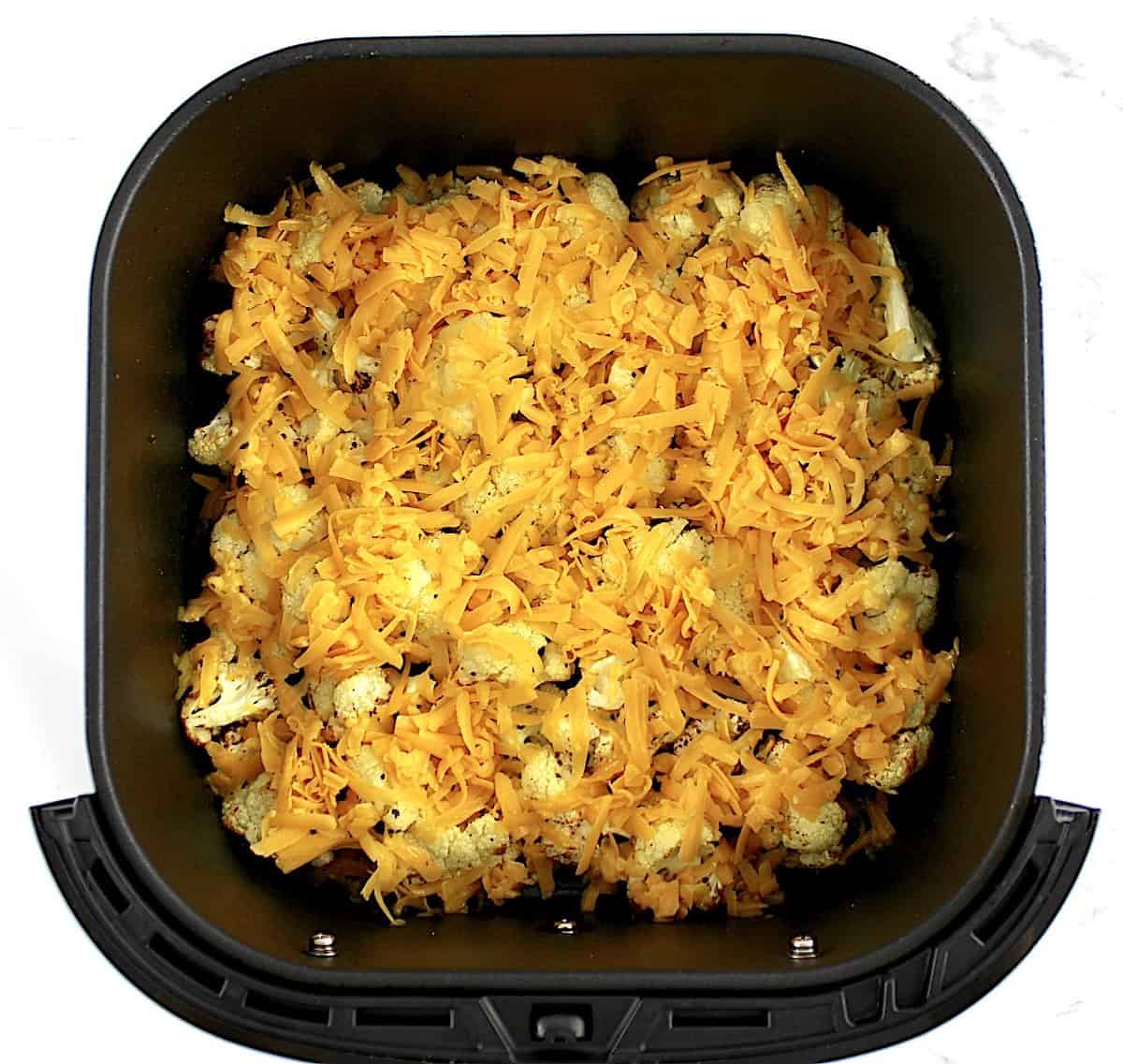 roasted cauliflower florets in air fryer basket with shredded cheddar cheese unmelted