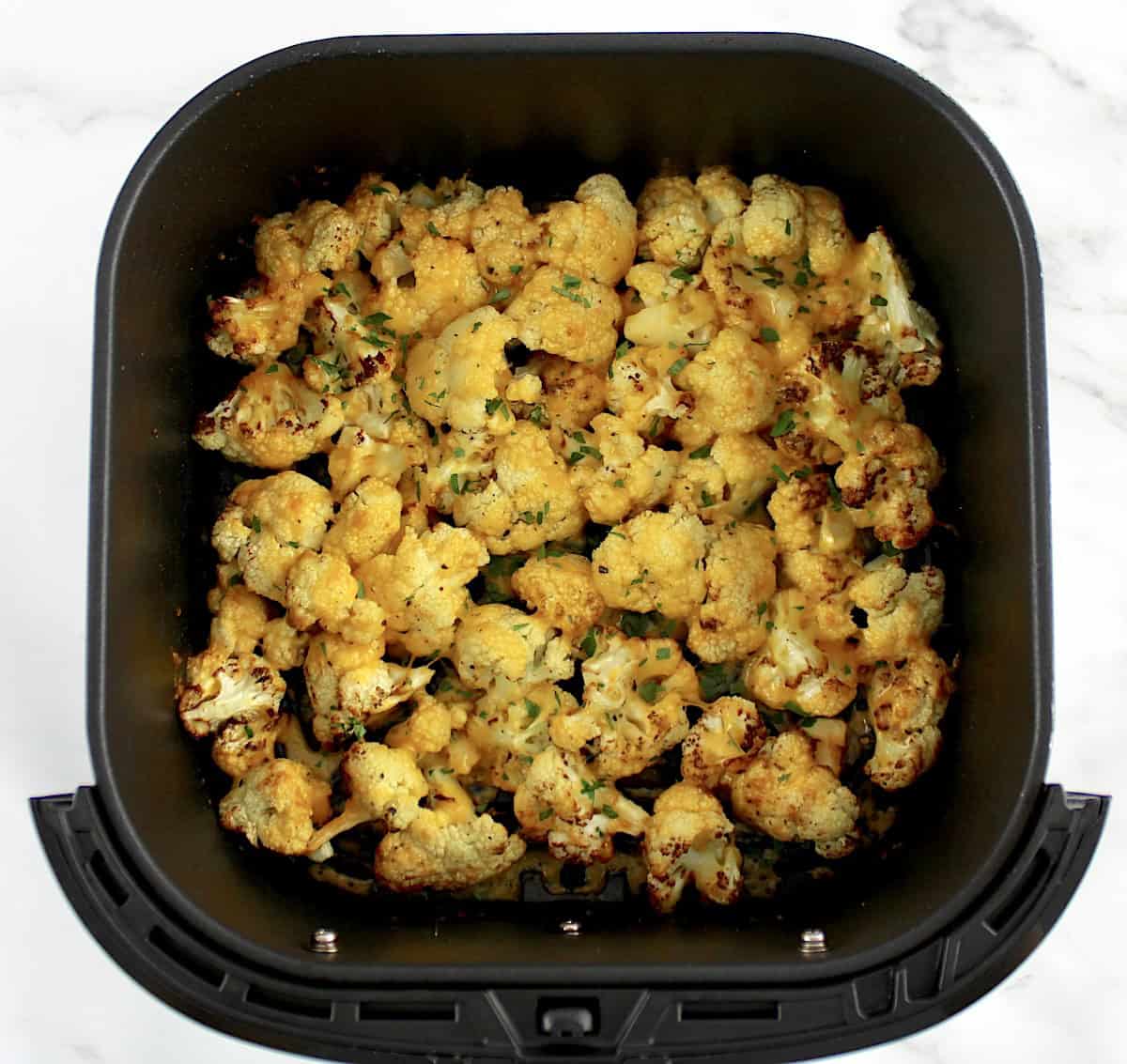 Air Fryer Cheesy Cauliflower in air fryer basket with chopped parsley on top