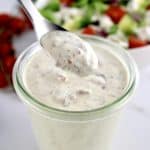 Bacon Ranch Dressing being spooned out of glass jar with salad in background