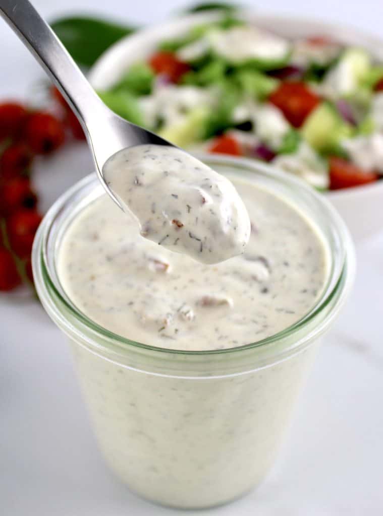 Bacon Ranch Dressing being spooned out of glass jar with salad in background