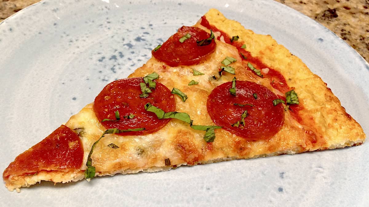 Cauliflower Pizza slice on plate with pepperoni and fresh basil sliced