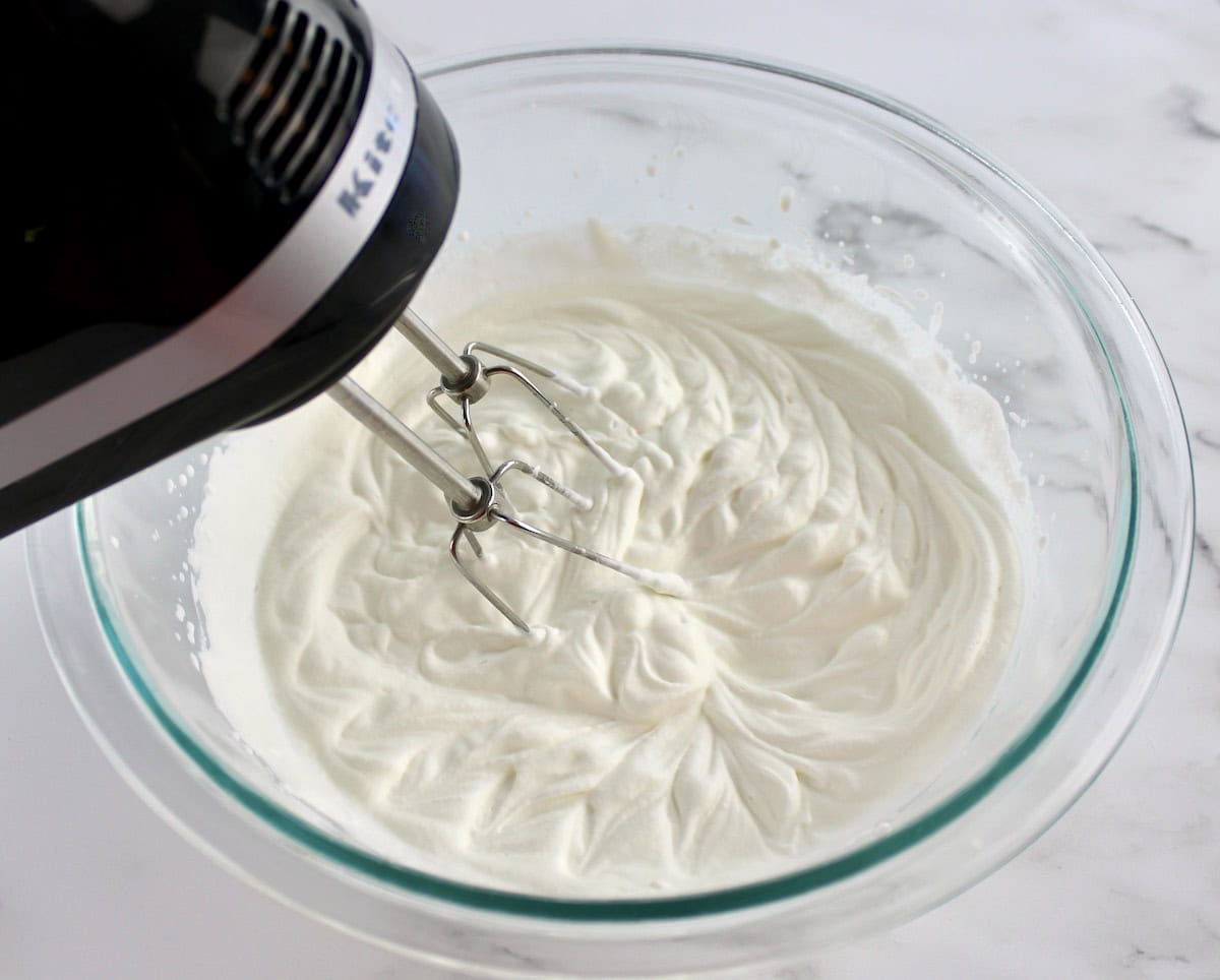 whip cream with hand mixer in glass bowl