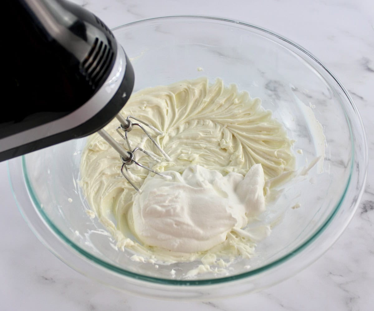 Easy Fruit Dip in glass bowl with dollop of whip cream and hand mixer