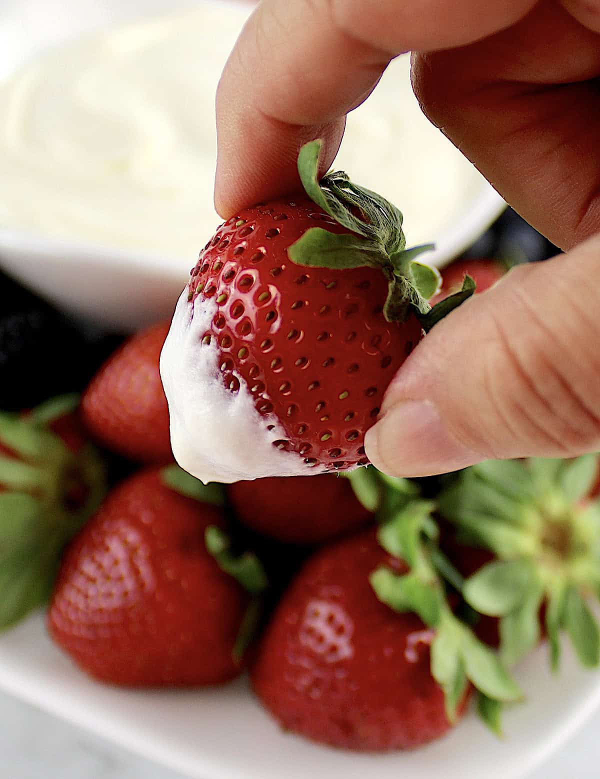 closeup of holding a strawberry with fruit dip on the end