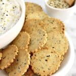 Everything Bagel Crackers on white plate with partial view of dip in white bowl