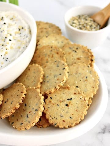 Everything Bagel Crackers on white plate with partial view of dip in white bowl