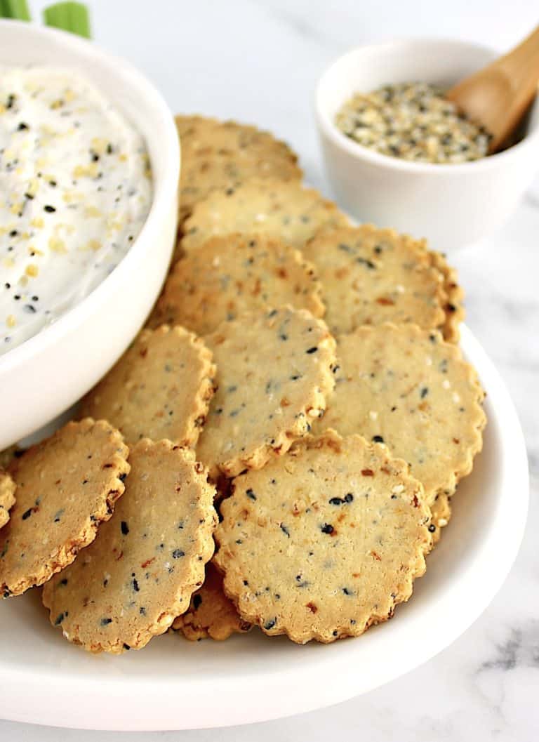 Everything Bagel Crackers on white plate with partial view of dip in white bowl